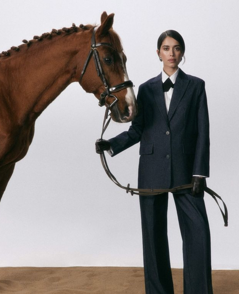 Person in equestrian attire standing next to a horse on a plain background